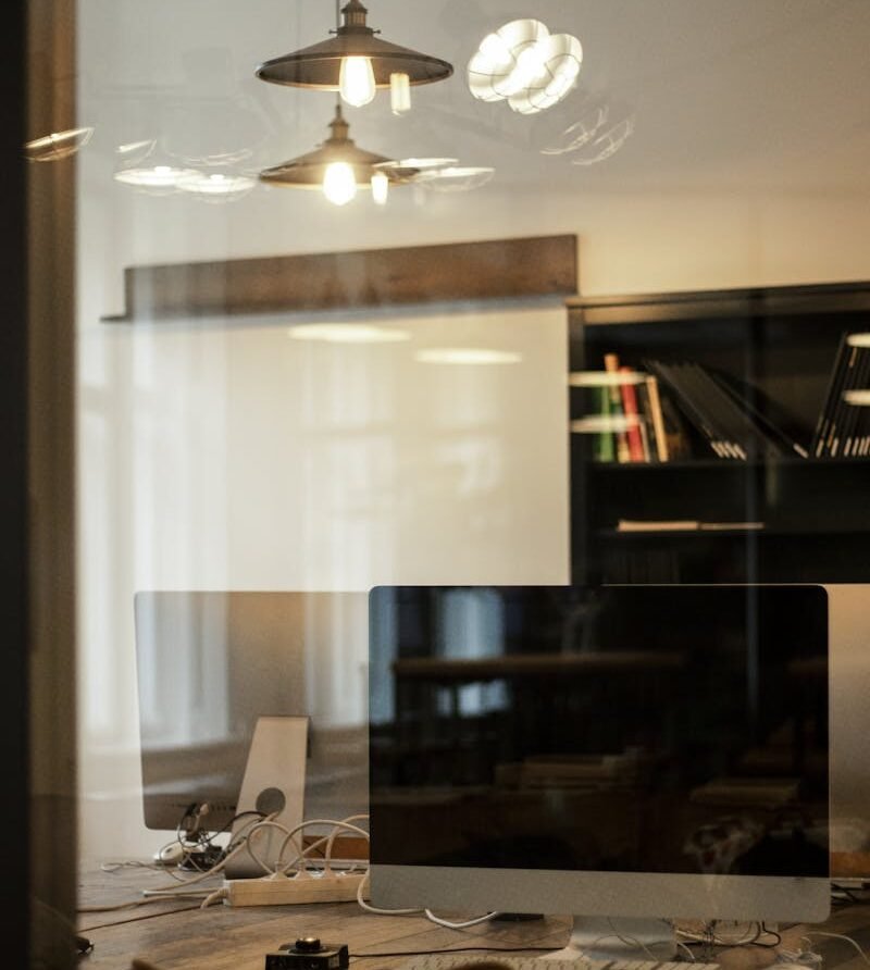 Stylish office setting featuring computers on a desk with elegant lighting fixtures and shelves.